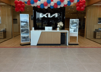 A reception desk at a Kia dealership, decorated with red, white, and blue balloons hanging from the ceiling above.