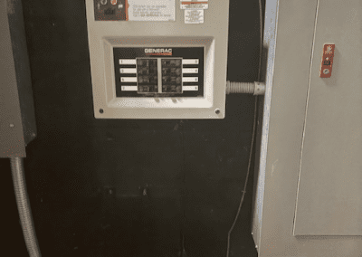 A Generac Home Link transfer switch panel is mounted on a wall, with a power cable coiled on a nearby surface.